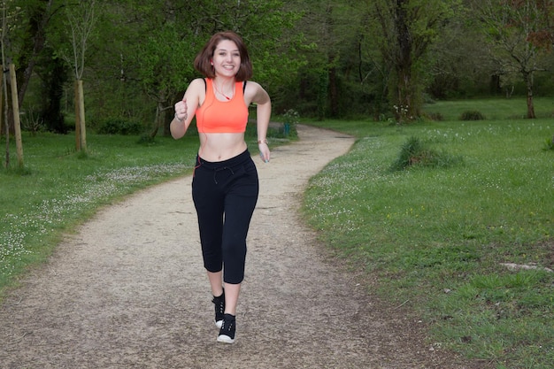 Sonriente mujer deportiva corriendo al aire libre en el parque