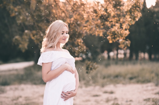 Sonriente mujer embarazada con elegante vestido blanco