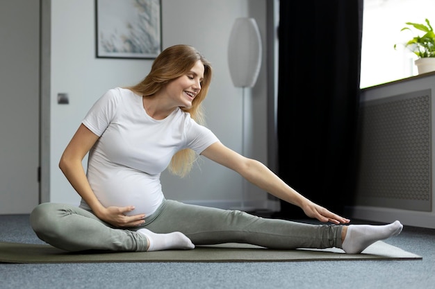 Sonriente mujer embarazada estirándose, haciendo ejercicios, practicando yoga en casa. concepto de embarazo