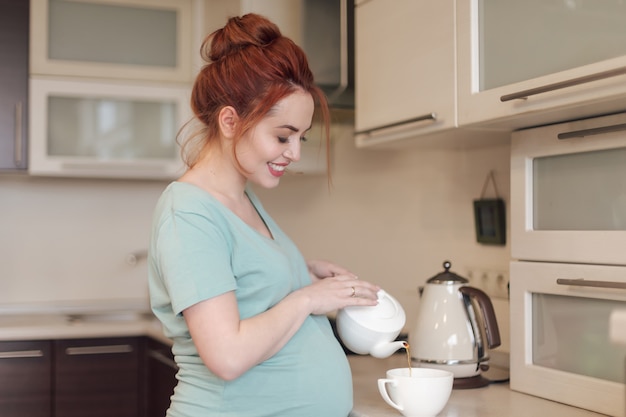 Sonriente mujer embarazada vertiendo té