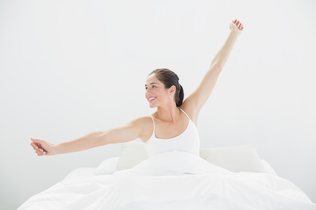 Sonriente mujer estirando los brazos en la cama