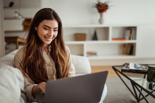 Sonriente mujer europea milenaria escribiendo en la computadora tiene chat y videollamada