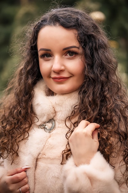 Sonriente mujer feliz de cabello rizado en un abrigo de pieles pasea por la feria del árbol de Navidad Esperando Navidad y Año Nuevo