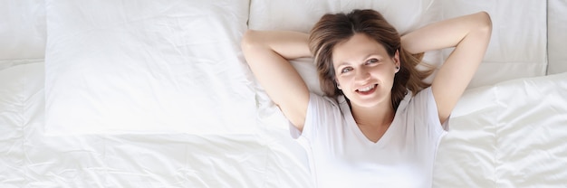 Sonriente mujer feliz se encuentra en la cama blanca, buen descanso y concepto de reglas de humor positivo