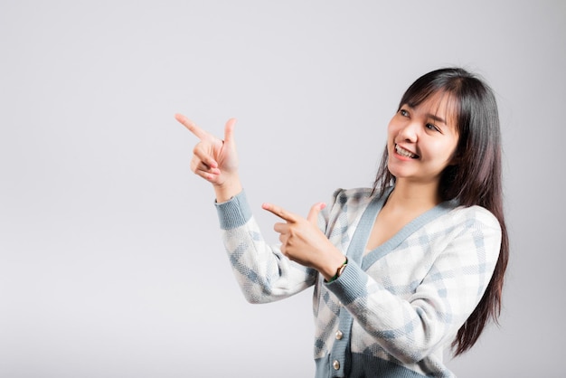 Sonriente mujer feliz señalando con el dedo el espacio, retrato asiático hermosa mujer joven punto en vacío mirando hacia un lado, tiro de estudio aislado sobre fondo blanco con espacio de copia