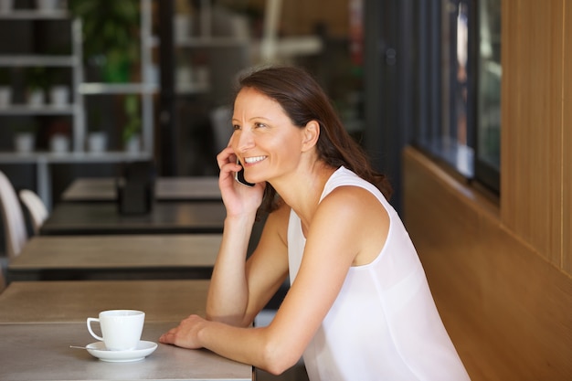 Sonriente mujer hablando por teléfono celular en el café