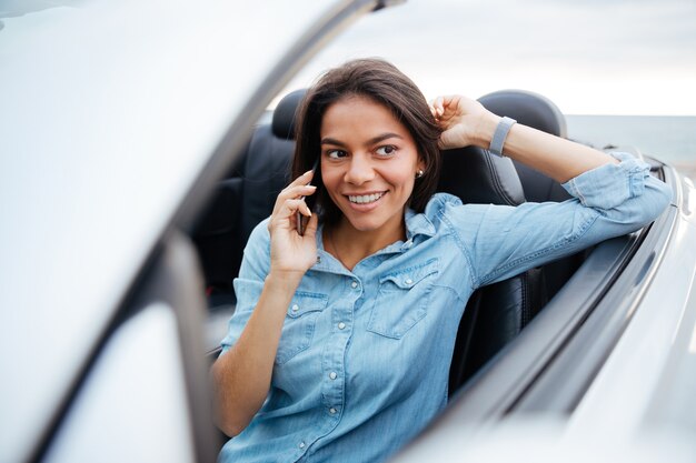 Sonriente mujer hermosa conduciendo coche y hablando por teléfono móvil