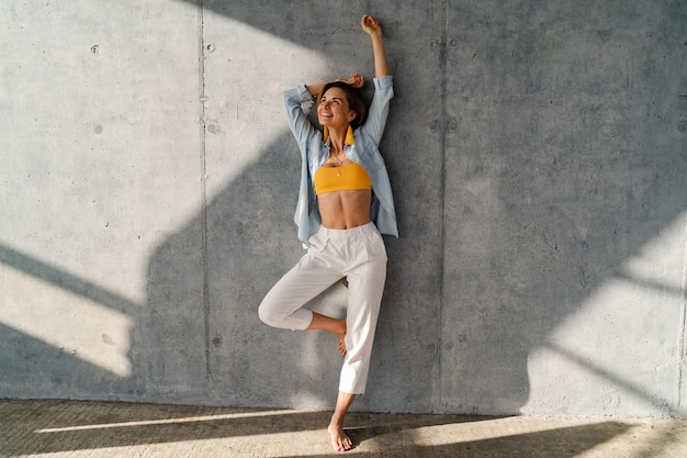 Sonriente mujer hermosa feliz posando contra la pared de hormigón en día soleado tendencia de estilo de moda de verano