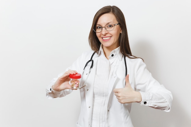 Sonriente mujer hermosa médico con estetoscopio, gafas mostrando los pulgares para arriba aislados sobre fondo blanco. Doctora en bata médica tiene botella con pastillas. Personal sanitario, concepto de medicina.