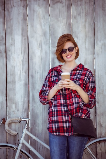 sonriente mujer hipster con café y una bicicleta, de pie