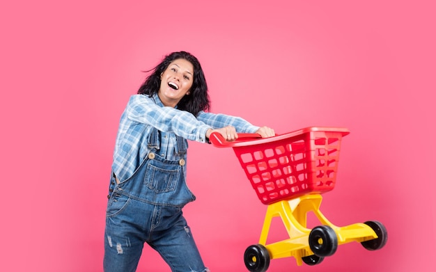 Sonriente mujer hipster con ropa de moda llevar carrito de compras ciber lunes