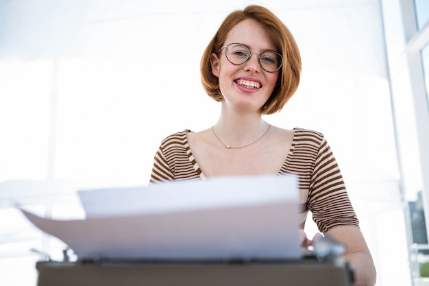 sonriente mujer hipster sentada en un escritorio, escribiendo en su máquina de escribir