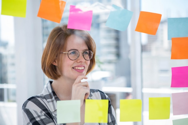 sonriente mujer hipster en su oficina, pegando notas a la pared