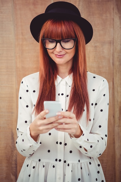 Sonriente mujer hipster usando su teléfono inteligente contra el fondo de madera