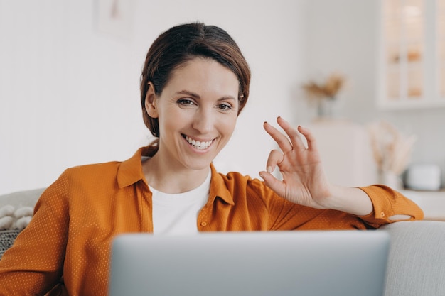 Foto sonriente mujer hispana mostrando bien sí gesto de acuerdo hablando por videollamada en la computadora portátil