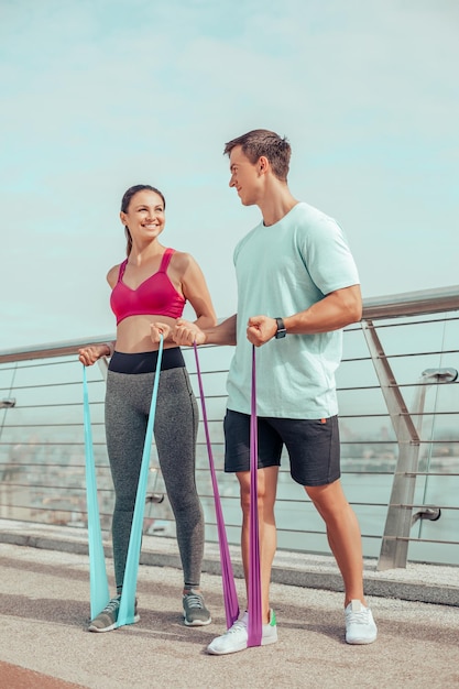 Sonriente mujer y hombre entrenando con bandas de goma en el puente