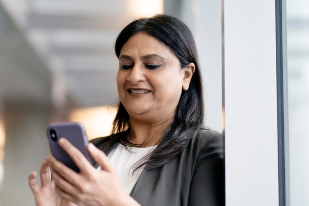 Sonriente mujer india madura sosteniendo un teléfono inteligente usando una aplicación móvil comprando en línea