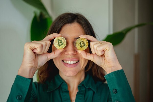 Sonriente mujer irreconocible que cubre sus ojos mostrando dos monedas bitcoin. Inversiones seguras en concepto de moneda virtual.