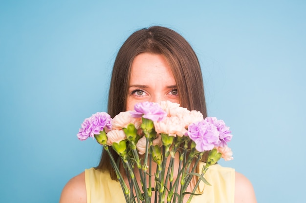 Sonriente a mujer joven y bonita con ramo de flores sobre fondo azul.