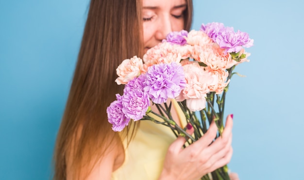 Sonriente a mujer joven y bonita con ramo de flores sobre fondo azul.