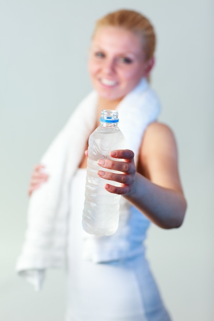 Sonriente mujer joven con una botella de agua y una toalla con enfoque en el agua