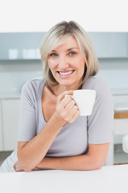 Sonriente mujer joven casual con taza de café en la cocina