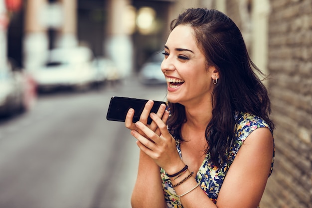 Sonriente mujer joven grabando nota de voz en su teléfono inteligente