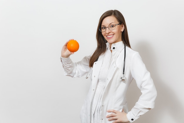 Sonriente mujer joven hermosa experimentada médico con estetoscopio, gafas aisladas sobre fondo blanco. Doctora en bata médica con naranja. El personal sanitario, la salud, el concepto de medicina.
