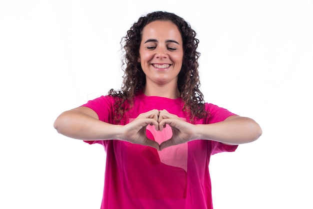 Foto sonriente a mujer joven positiva con camiseta rosa haciendo forma de corazón con las manos.