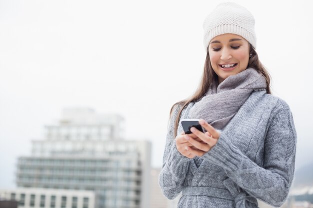 Sonriente mujer joven con ropa de invierno en mensajes de texto