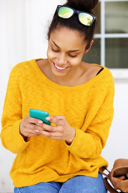 Sonriente mujer joven sentada afuera usando teléfono móvil