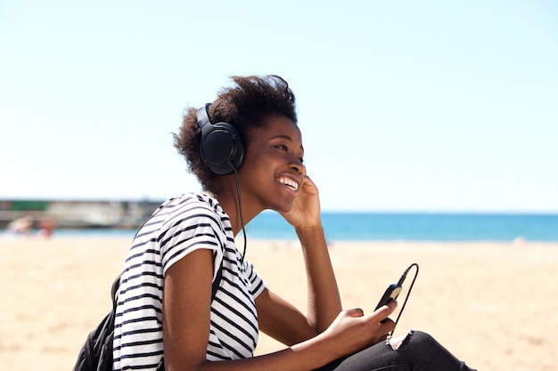 Sonriente mujer joven sentada al aire libre y escuchando música con auriculares