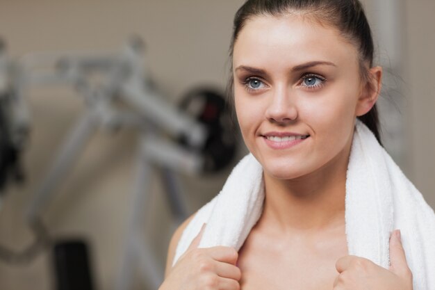 Sonriente mujer joven con una toalla alrededor del cuello en el gimnasio