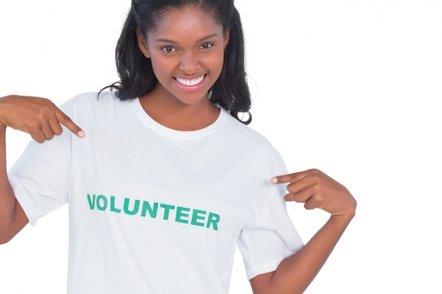 Sonriente mujer joven vistiendo camiseta voluntaria y apuntando a ella