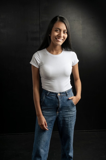 Sonriente mujer latina de pelo negro vistiendo un jean y una camiseta blanca sobre un fondo negro