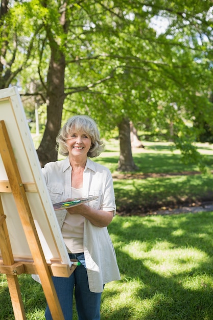 Sonriente mujer madura pintura sobre lienzo en el parque