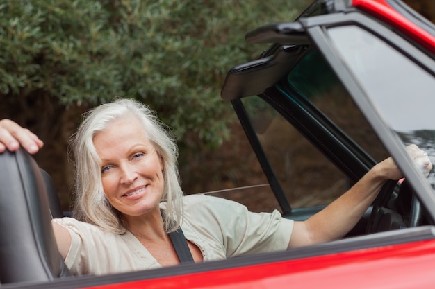 Sonriente mujer madura posando en convertible rojo