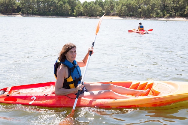 Sonriente mujer de mediana edad en kayak en un lago.