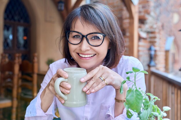 Sonriente mujer de mediana edad con un vaso de cerveza kvass mirando a la cámara relajándose sentado en un pub al aire libre Café Bebidas de ocio turismo de verano concepto de personas de mediana edad