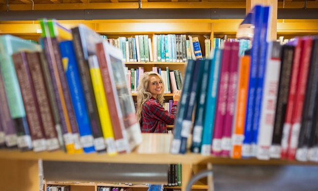Sonriente mujer en medio de estantes en la biblioteca