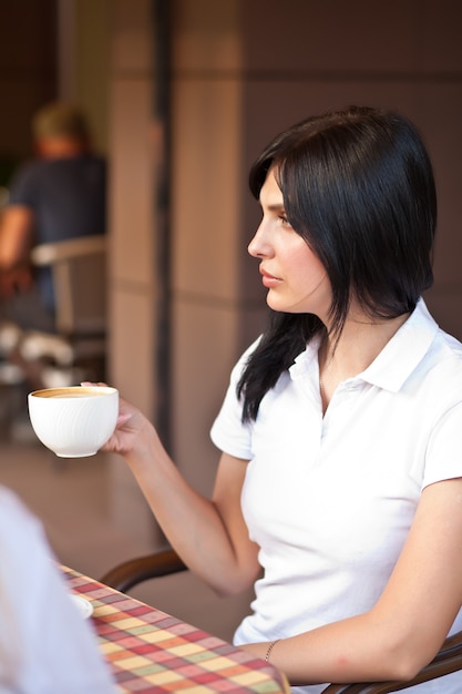 Sonriente mujer morena en la cafetería tomando café con croissant. Concepto de comunicación y amistad.