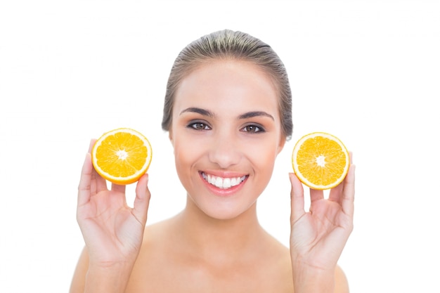 Sonriente mujer morena con dos mitades de naranjas