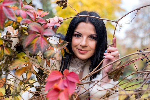 Sonriente mujer morena con ramas de árboles en el parque otoño