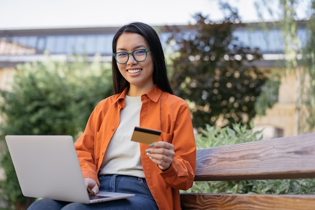 Sonriente mujer de negocios asiática con tarjeta de crédito usando una computadora portátil comprando en línea