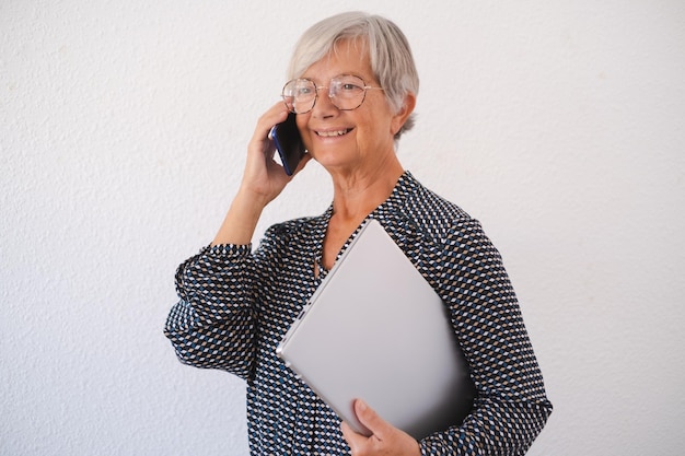 Sonriente mujer de negocios hablando por teléfono móvil aislado sobre fondo blanco Señora mayor sosteniendo la computadora portátil bajo el brazo