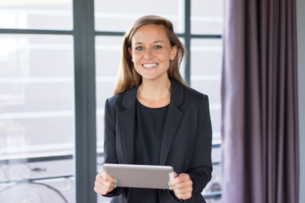 sonriente mujer de negocios hermosa joven mirando a cámara, sosteniendo la tableta