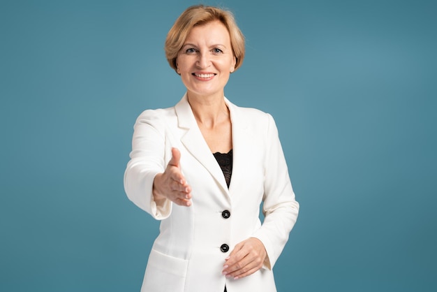 Sonriente mujer de negocios madura que ofrece apretón de manos mientras presenta aislado sobre el fondo azul. Foto de stock