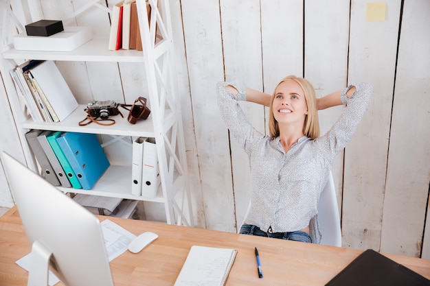 Sonriente mujer de negocios preguntada descansando mientras está sentado en una silla en su lugar de trabajo