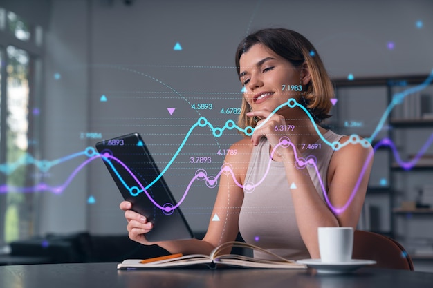 Sonriente mujer de negocios en ropa casual sosteniendo un dispositivo de tableta tocándolo en el lugar de trabajo de la oficina Concepto de trabajo distante educación empresarial tecnología de la información Gráfico de Forex y holograma gráfico