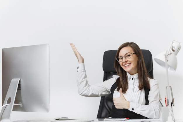 Sonriente mujer de negocios sentada en el escritorio, trabajando en equipo con documentos en la oficina de luz